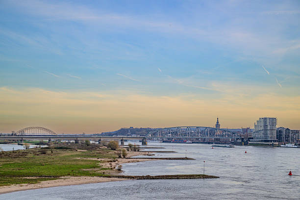 Skyline of the city Nijmegen on the riverbank of the Waal river during sunset. Various ships are passing the river during this beautiful cold winter afternoon.