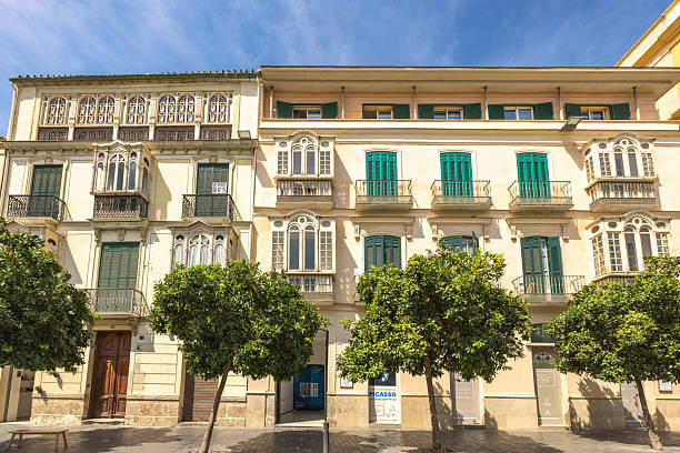 Malaga, Spain - September 12, 2024: Charming European architecture with lush green trees lining a sun-drenched street.