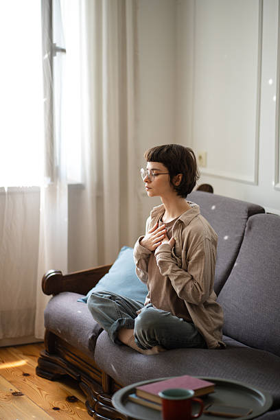 istock Young woman sitting on sofa practicing meditation, doing breathing exercises for calming thoughts. 2251141701
