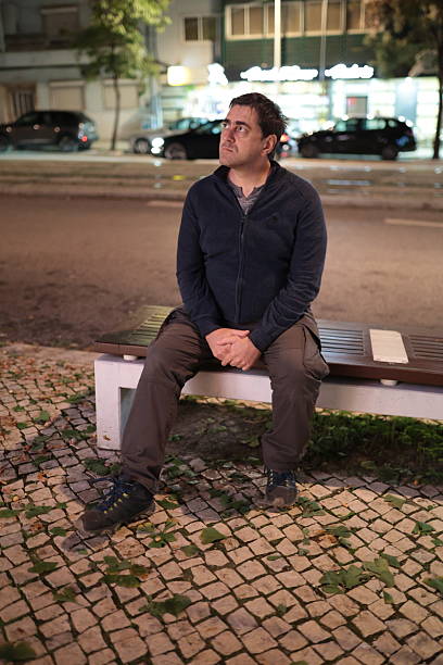 istock Young man sitting on bench feeling thoughtful at night 2251141898