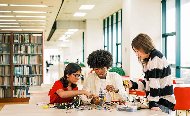 istock Three diverse studentsAfrican, Indian, and Asiancollaborate on a robotics project at a library table, surrounded by books and windows, showcasing teamwork, creativity, and academic innovation. 2251142786