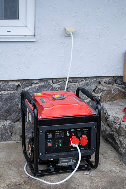 istock Red portable generator operating outdoors, providing power to a residential structure via a connected electrical cord 2251146264