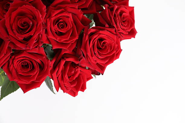 This vibrant still life depicts a bouquet of deep red roses in a tall glass vase on a round wooden surface, against a light background. The flowers symbolize love and romance, and the contrast of colors adds solemnity and elegance to the image.