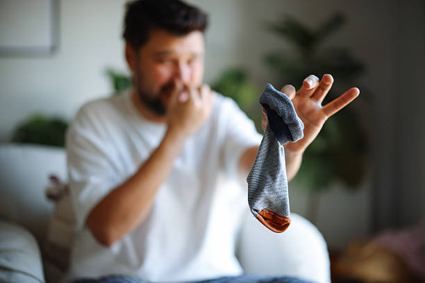 istock A man makes a disgusted face after sniffing a dirty sock while sitting on a couch in a casual setting 2251153250