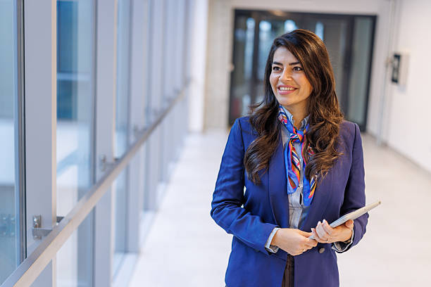 istock Woman smiling while walking in a corporate hallway carrying a tablet for work 2251156197