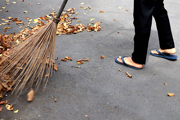A male sanitation worker sweeping autumn leaves on the road in Bangkok, Thailand