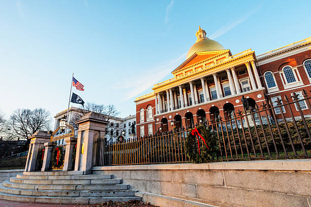 Boston, Massachusetts, USA - December 6, 2025:  A winter sun setting on the Massachusetts State House. The Massachusetts State House, also known as the Massachusetts Statehouse or the New State House, is the state capitol and seat of government for the Commonwealth of Massachusetts, located in the Beacon Hill neighborhood of Boston. The building houses the Massachusetts General Court (state legislature) and the offices of the Governor of Massachusetts. The building, designed by architect Charles Bulfinch, was completed in January 1798 and has repeatedly been enlarged since. It is one of the oldest state capitols in current use. It is considered a masterpiece of Federal architecture and among Bulfinch's finest works, and was designated a National Historic Landmark for its architectural significance.