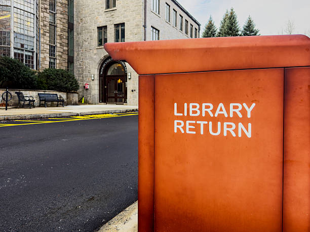 Winchester, Massachusetts, USA - December 4, 2025: An orange library book return container in the parking lot of the Winchester Public Library. Selective focus.