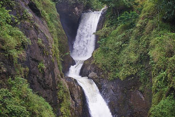 Majestic multi–tier waterfall flowing through lush green cliffs in a tropical rainforest.