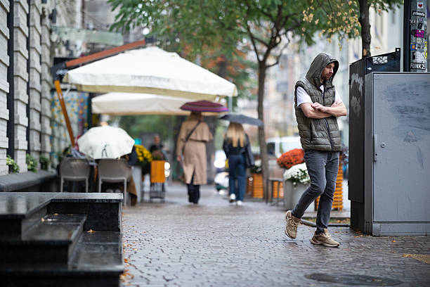 Kyiv, Ukraine - October 5, 2024: Man wearing green vest and hood walking on wet pavement of Yaroslaviv Val street. Autumn rainy weather lifestyle in the city.