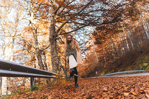 A young woman walks along an autumn path, smiling as she enjoys the crisp air and falling leaves. A warm, cozy, and cinematic fall vibe fills the entire scene.
