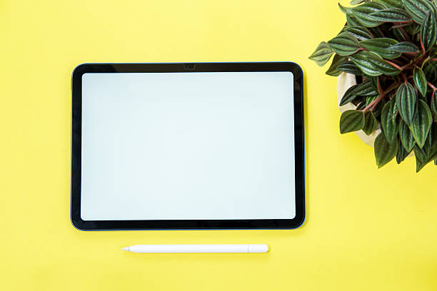 Digital tablet with a blank white screen and pen on a yellow background.