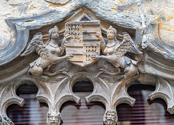 Ornate stone carving of griffin-like creatures holding a shield on an ancient building facade.