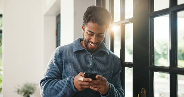 istock Window, typing and happy man with phone, browsing internet and check social media post. Message notification, texting and person in home with mobile app, online communication and reply to comment. 2251176299