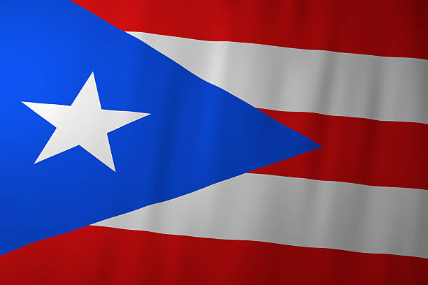 The image shows the national flag of Puerto Rico, featuring five alternating red and white stripes and a blue triangle pointing inward with a single white star. The gently waving fabric highlights the bold colors and iconic Caribbean design.