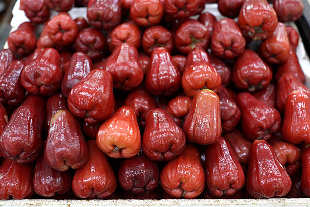 A close-up view of fresh red wax apples neatly stacked at a market stall, highlights the glossy texture, vibrant color, and natural freshness of this tropical fruit, commonly found in Southeast Asian markets and enjoyed as a healthy snack.
