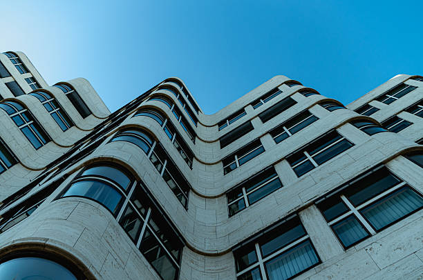 Berlin, Germany – August 6, 2018: Low angle view of the Shell-Haus office building near the Landwehr Canal, showing its characteristic curved travertine facade and horizontal rows of windows under a clear blue sky.
