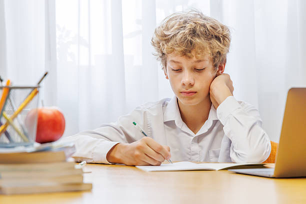 istock Schoolboy sitting at home, with focus and concentration while doing homework 2251194544
