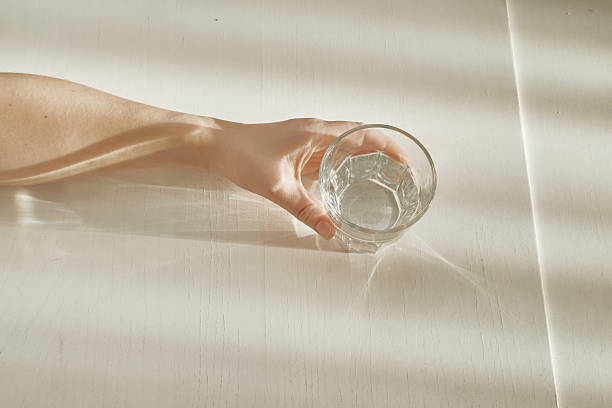 istock Hand holding glass of refreshing water on table with sun shadows 2251198656