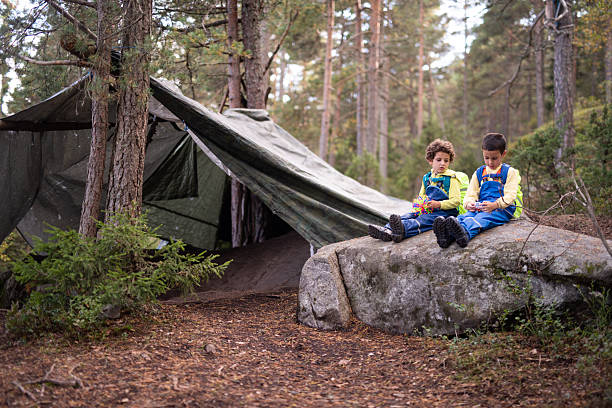 istock Boys sitting on rock playing outside makeshift tent in forest. 2251199386