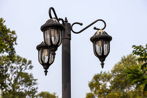 Close-up of a classic black, three-head outdoor post light constructed from durable cast aluminum, standing against a bright sky. Design for street lighting, garden, and park pathways.