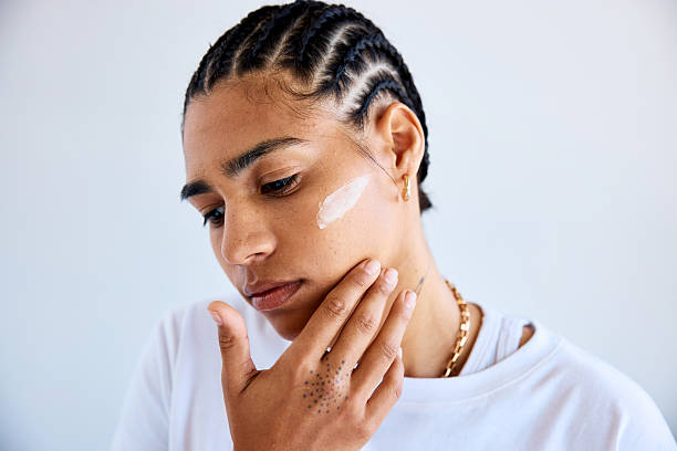 istock Closeup studio shot of thoughtful young person with black cornrows touching face while applying beauty cream 2251199971