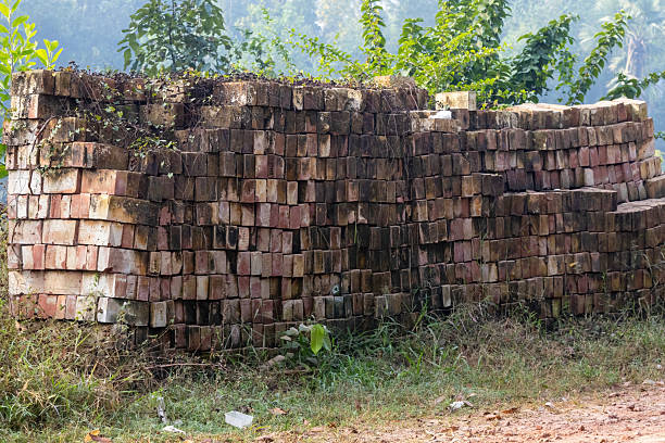 Stacks of orange and brown bricks are neatly piled at a construction site, glowing warmly under the sunset light.