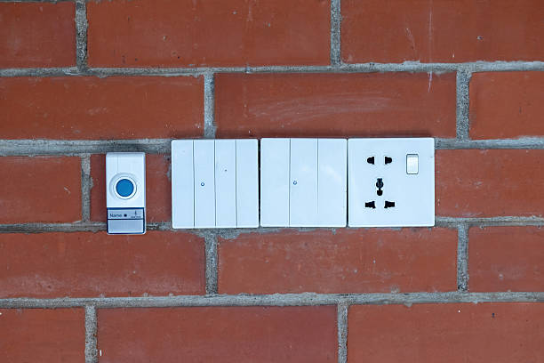 A set of functional electrical fixtures, including a 3-pin power socket and a 4-gang light switch unit, professionally installed and recessed into a vintage, textured red brick wall surface.
