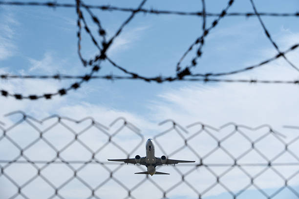 istock White Airplane Behind Barbed Wire Fence Against Blue Sky 2251209700