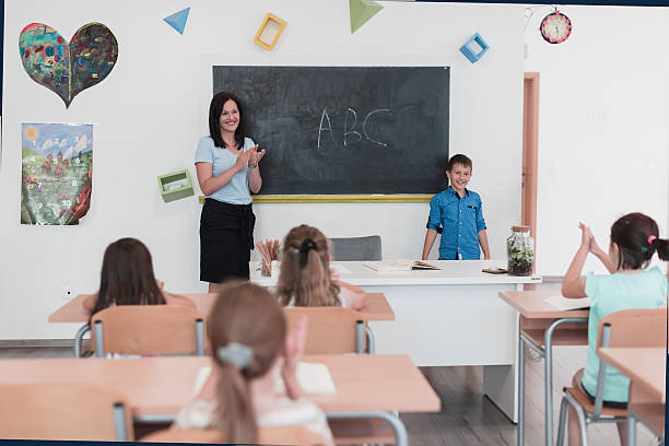 istock Elementary school. The female teacher helping the child student while writing the answer on the chalkboard. 2251210613