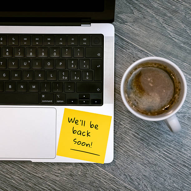 istock We will be back soon Away Message on a Yellow Sticky Note on a Laptop Next to a Coffee Mug 2251211084
