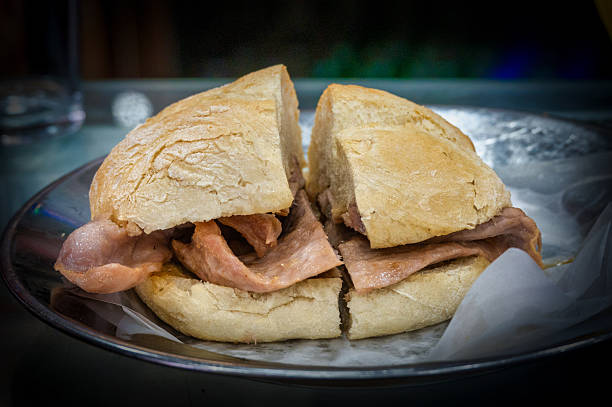 Close up of a traditional Portuguese bifana sandwich served on a plate, with slices of pork in fresh bread.