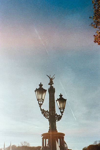 A decorative historic lamppost rises superimposed  in front of the Victory column at  Platz der Republik, creating a new composition. The scene exudes nostalgia and elegance against blue sky.