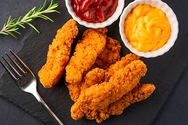 istock Fried chicken breast strips on black table background. Delicious chicken crisps 2251228916