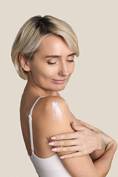 istock Caucasian Middle Aged Woman Applying Moisturizer to Shoulder Smiling Gently 2251229475