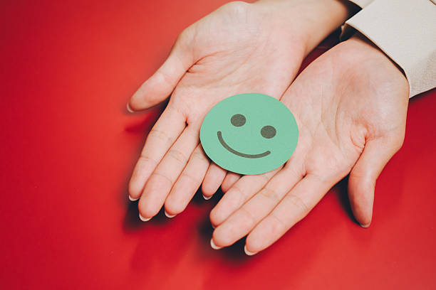 istock Feedback concept. Smiling face cutout on open hands with red background, symbolizing happiness and positivity in simple and warm composition 2251235974