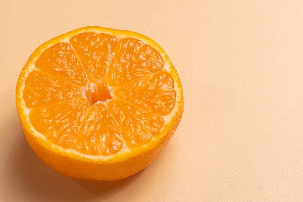 istock Single orange half showing glossy segments on a clean beige background. 2251237379
