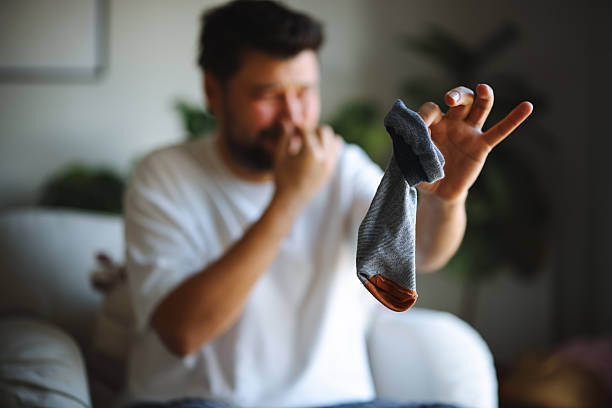 istock A man makes a disgusted face after sniffing a dirty sock while sitting on a couch in a casual setting 2251242851