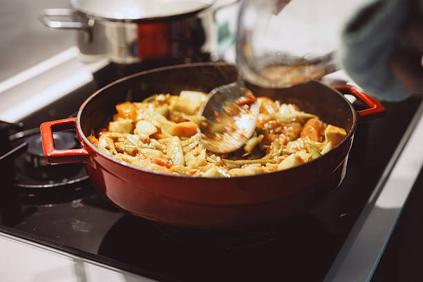 Beautiful smiling caucasian blond young woman standing in kitchen and stirring soup in pot. Cooking Traditional Turkish Vegan Carrot and Leek Vegetable in saucepan.
