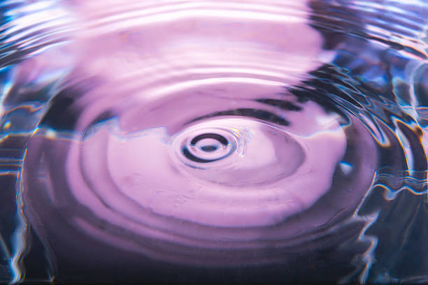 316.An abstract, intense close-up of a pink and purple liquid surface. A water drop impact creates perfectly circular ripples and a splash, reflecting a serene and clean feel with vibrant tones.