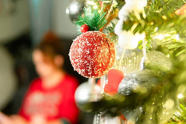 istock Christmas ornament hanging on decorated tree with person in background 2251247368