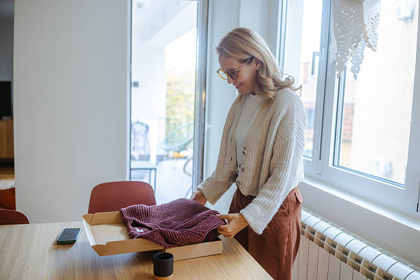 istock Woman unboxes a knit sweater from a parcel at home, standing by a sunlit window 2251247536