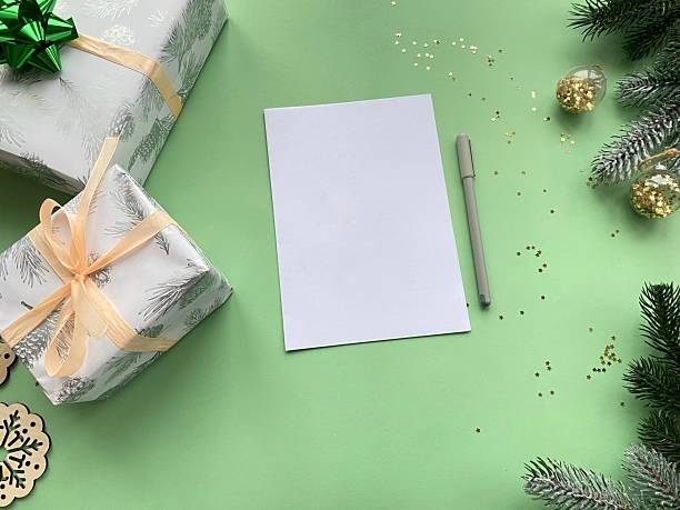 istock Holiday flat lay with gift boxes, evergreen branches and a blank white paper sheet with a pen on a light green backdrop. Blank layout for text or design 2251248500