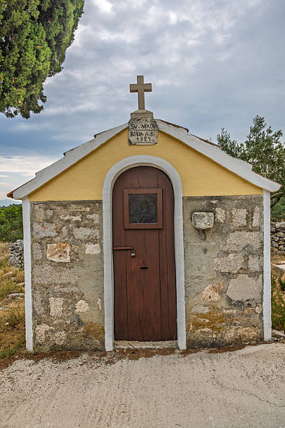 istock Serene Chapel Beside Tall Cypress Tree Under Cloudy Sky in Rustic Mediterranean Countryside 2251248670