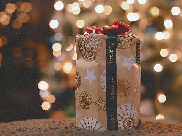 Cozy Christmas gift wrapped in unique pattern paper and red ribbon under the festive tree. Captures the authentic holiday atmosphere, joy of giving, and magic of New Year 2026 at home. Feliz Navidad.
