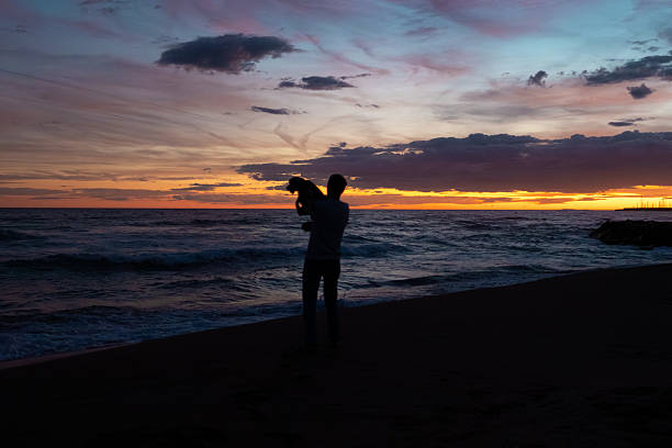 Man and his loyal dog enjoying a peaceful moment together on the beach during twilight, with a beautiful colorful sky creating a silhouetted scene of companionship and love