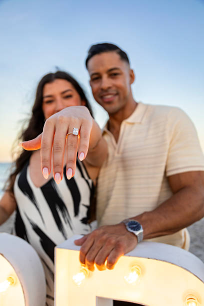 istock A newly engaged woman proudly shows her engagement ring while standing with her partner on a beach at sunset. 2251256210