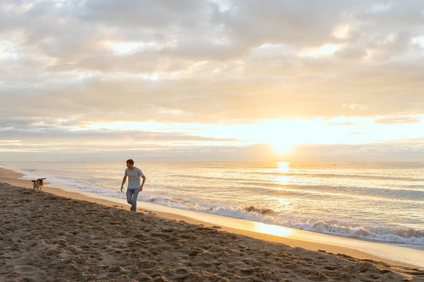 istock Man and dog walking on beach at sunrise 2251256236