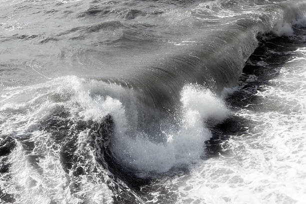 Powerful ocean wave crashing against the shore, creating a frothy spray of white water, showcasing the dynamic movement and energy of the sea in a dramatic coastal scene