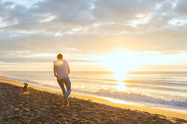 istock Man and dog running on beach at sunrise 2251256520